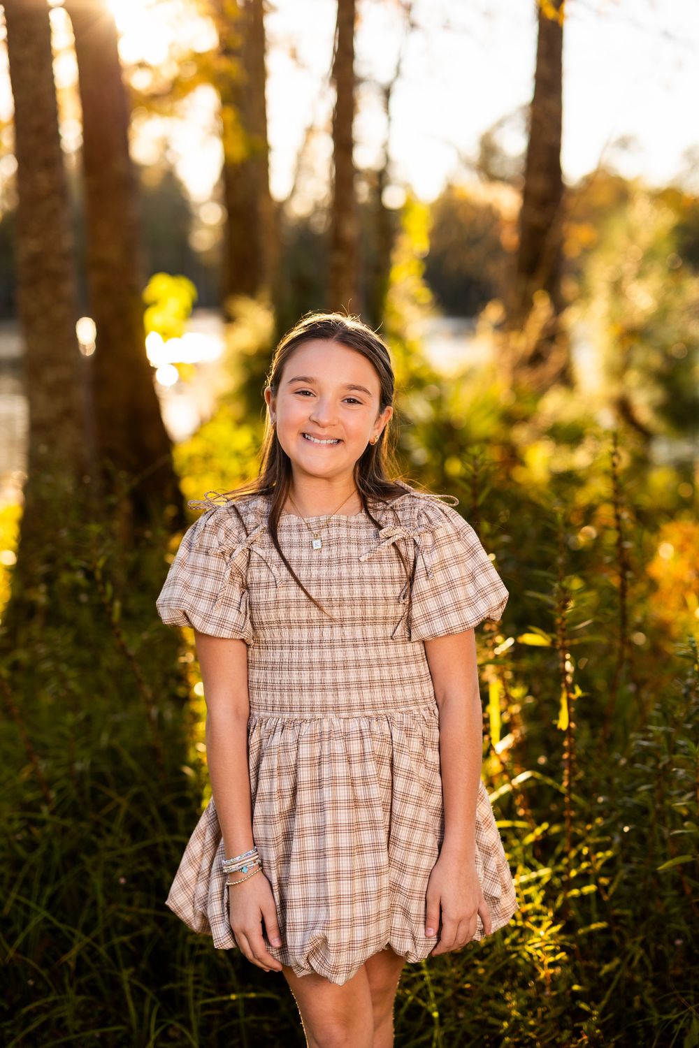 Golden hour portrait in a forest setting wearing plaid dress with sunlit background.