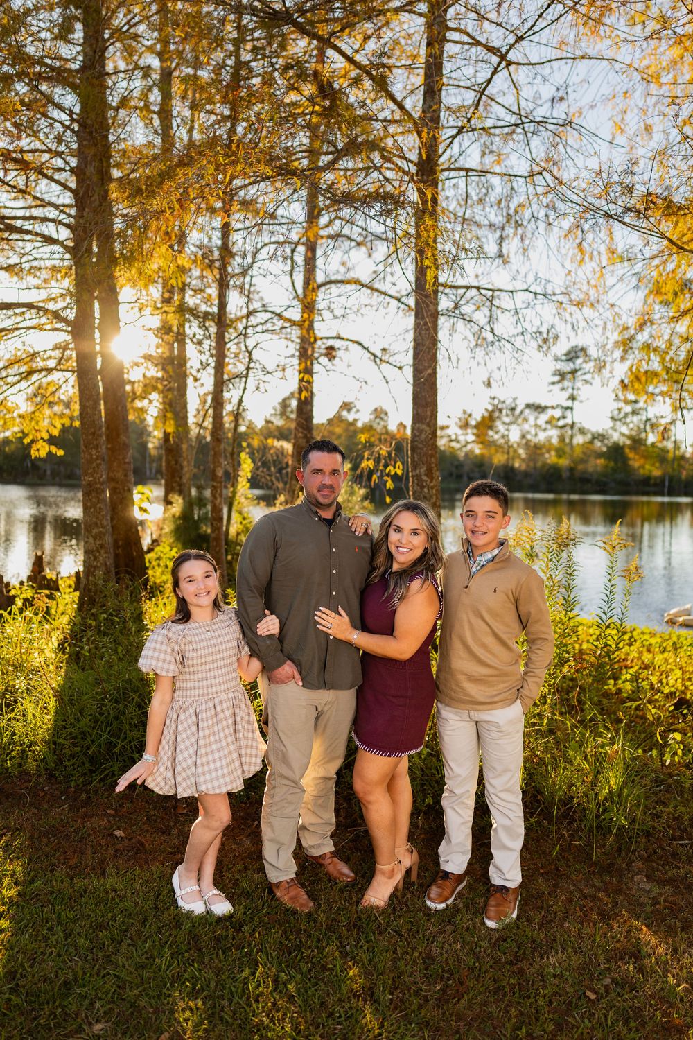 Family poses together by a lake during golden hour autumn photoshoot with trees and water in background.