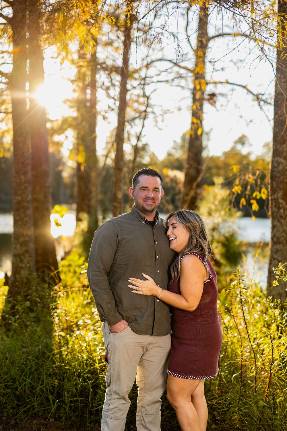 Couple shares intimate moment during sunset photoshoot by lake with autumn foliage.