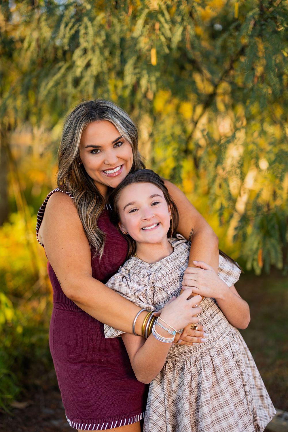 Mother and daughter share joyful embraces during outdoor fall photoshoot with golden lighting.