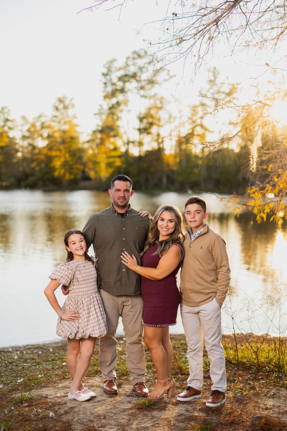Family group poses casually by lakeside during fall sunset with trees in background.