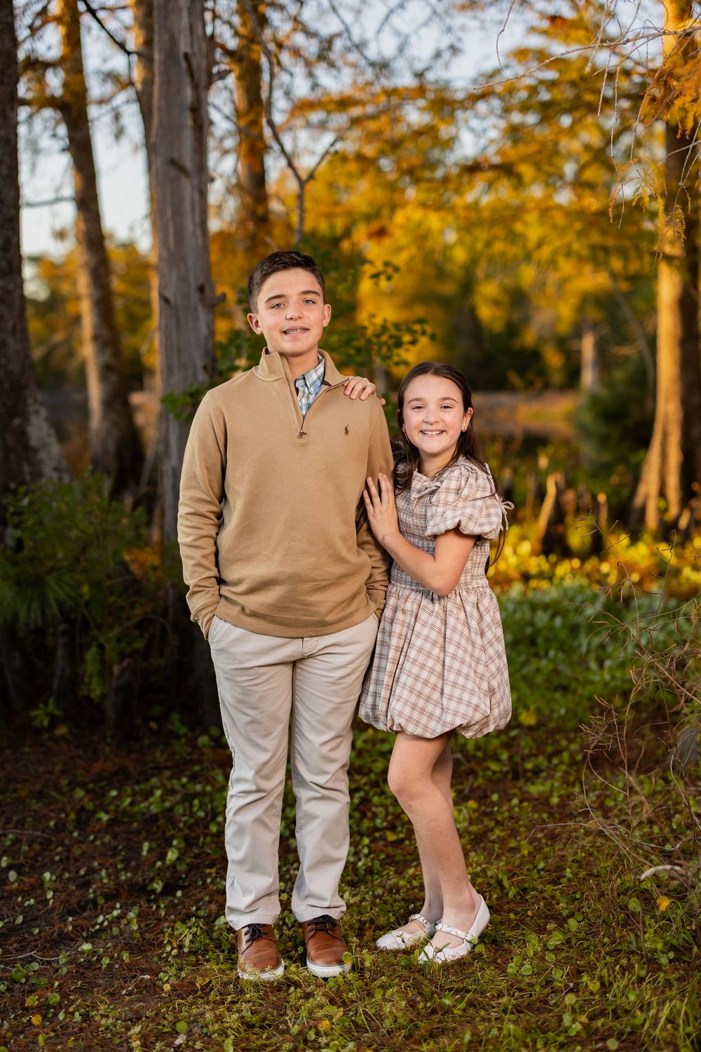 Two people share warm smiles while posing outdoors in autumn setting with golden light.