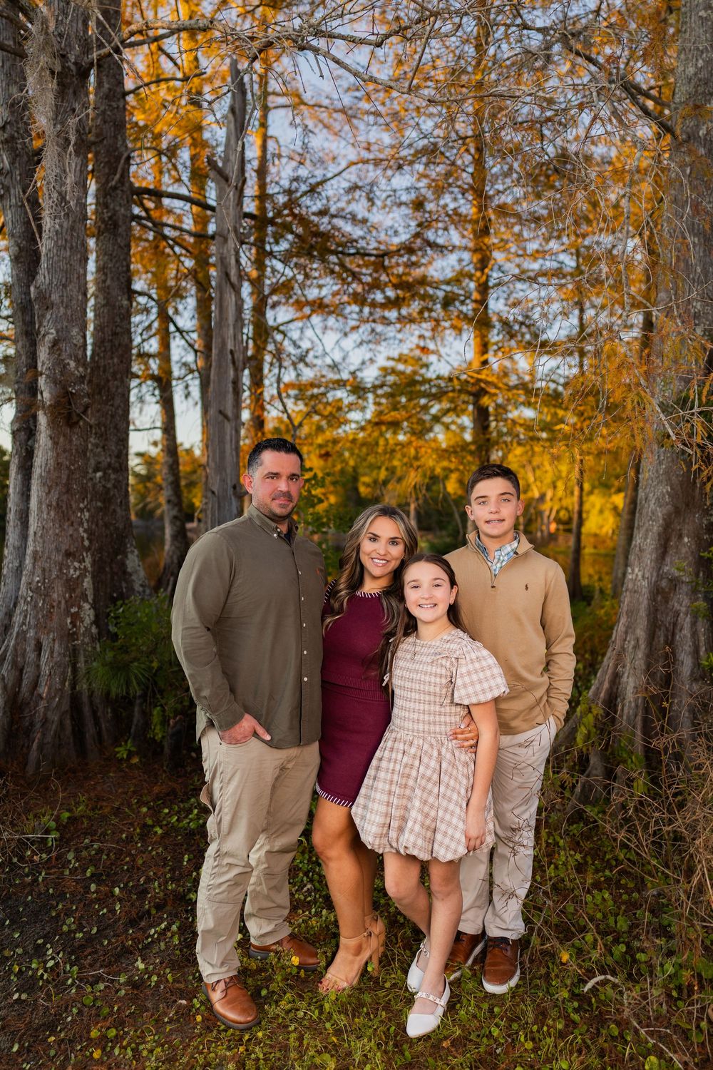 Family group poses casually in wooded area with golden autumn foliage.