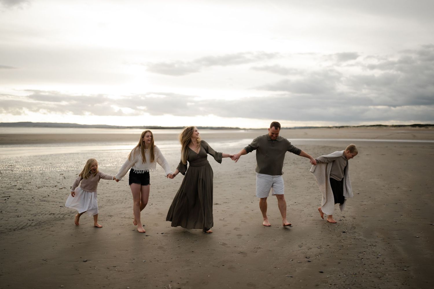 a family of five waking on the beach and laughing while holding hands, kent family photographer