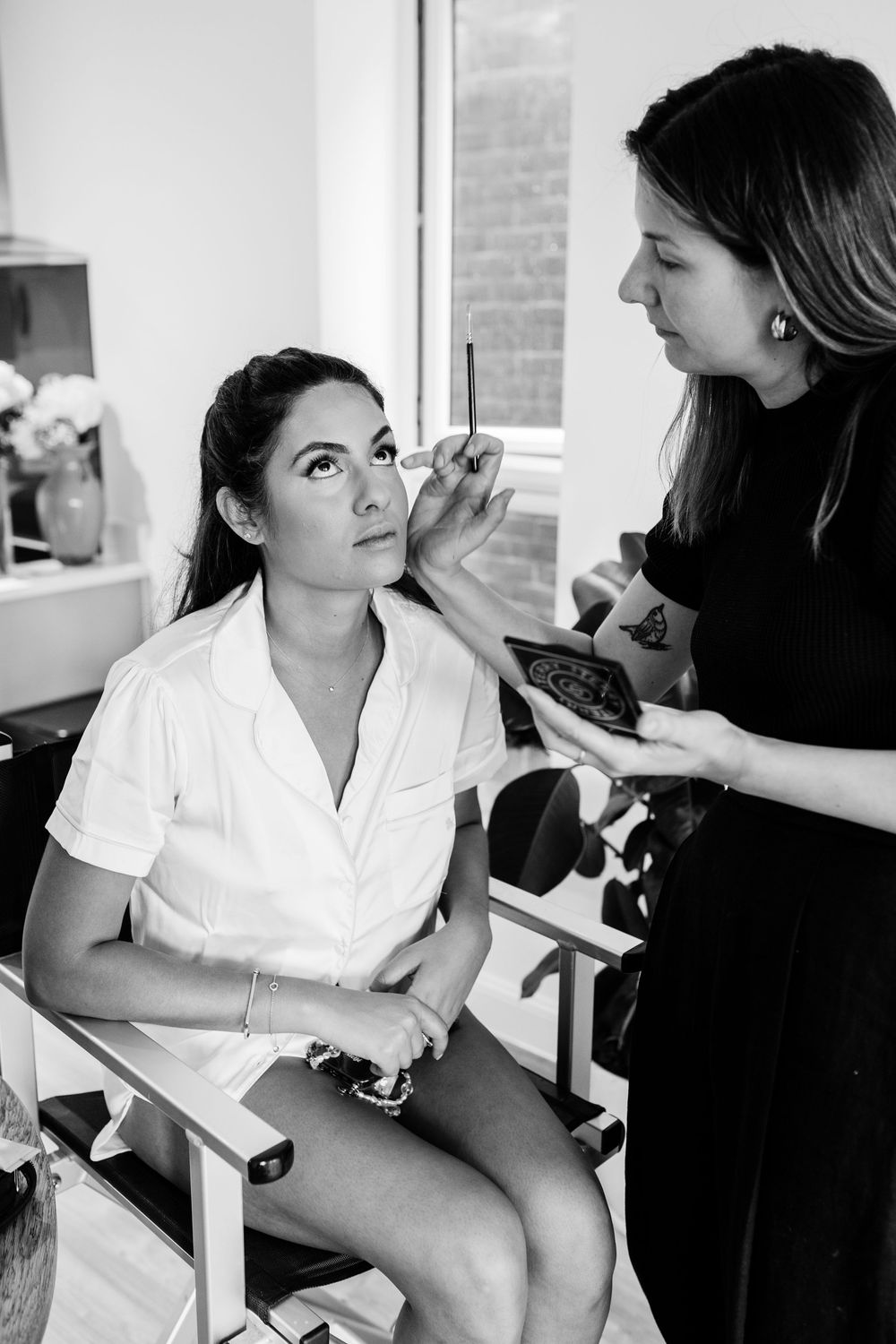 Black and white photos showing bridal makeup preparation in natural window light.