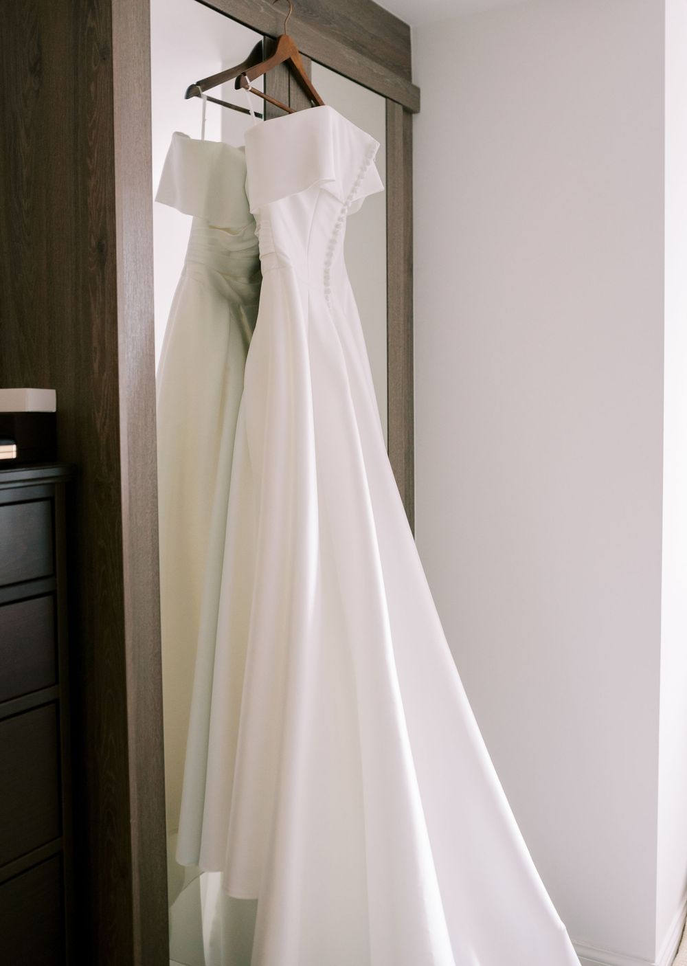 Elegant white wedding dress hanging on display in a minimalist room.