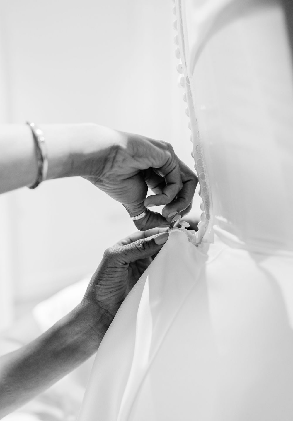 Close-up details of hands making final adjustments to a white wedding dress.