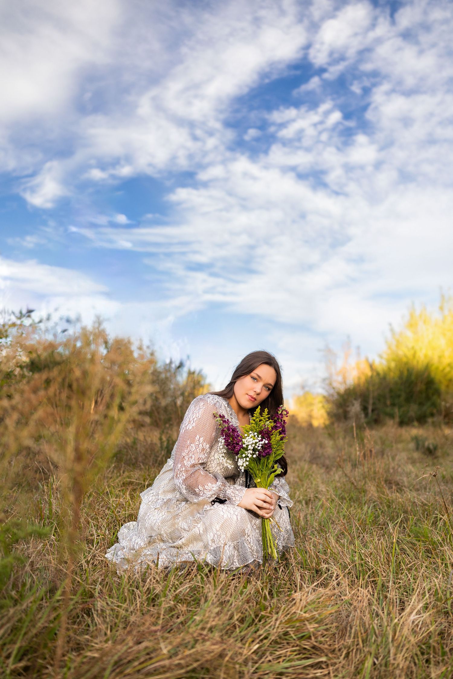 Dreamy outdoor photography session in a meadow with tall grass and cloudy skies.