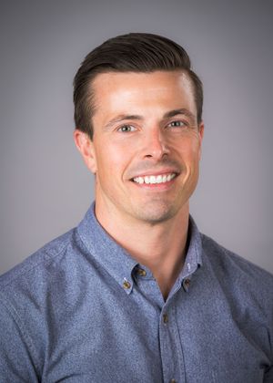 Professional headshot of someone wearing a blue button-down shirt against a gray background.