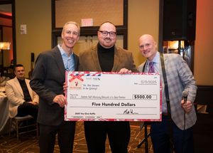 A group of people stand together holding large ceremonial checks at what appears to be an awards or presentation event.