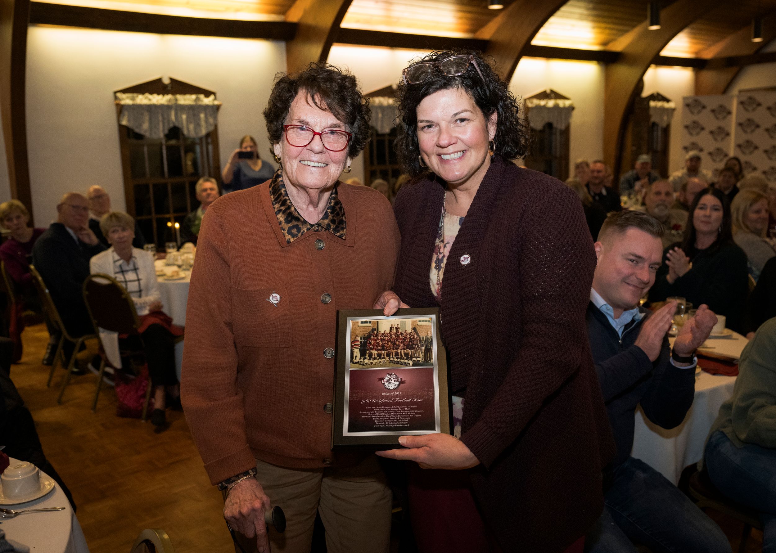 People gathered at an indoor event with warm lighting and awards or plaques being displayed in a celebratory setting.