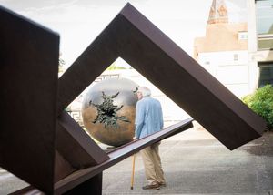 A sequence of photographs showing a person walking past a large angular metal sculpture mounted on a concrete wall.