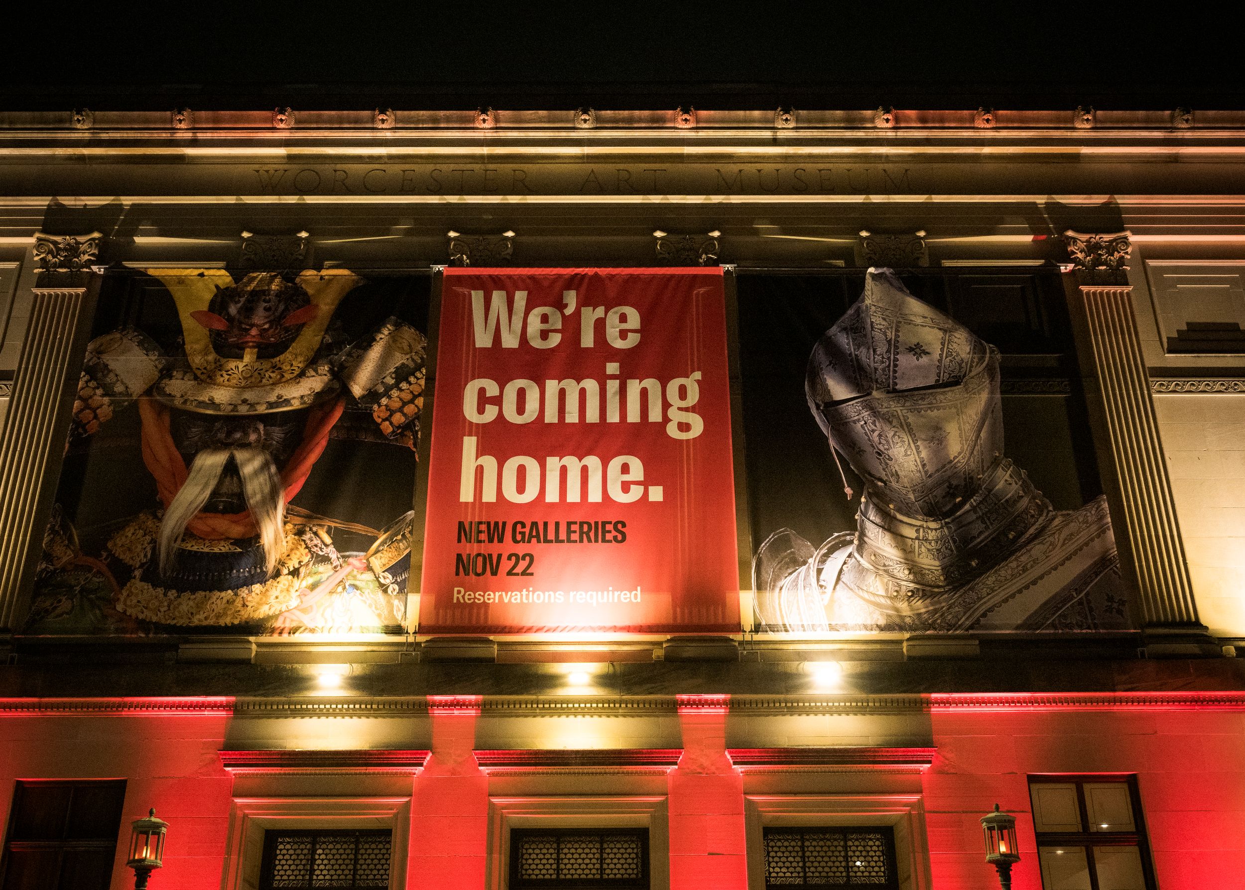 A red banner reading 'We're coming home' illuminated at night on a building facade with decorative elements.