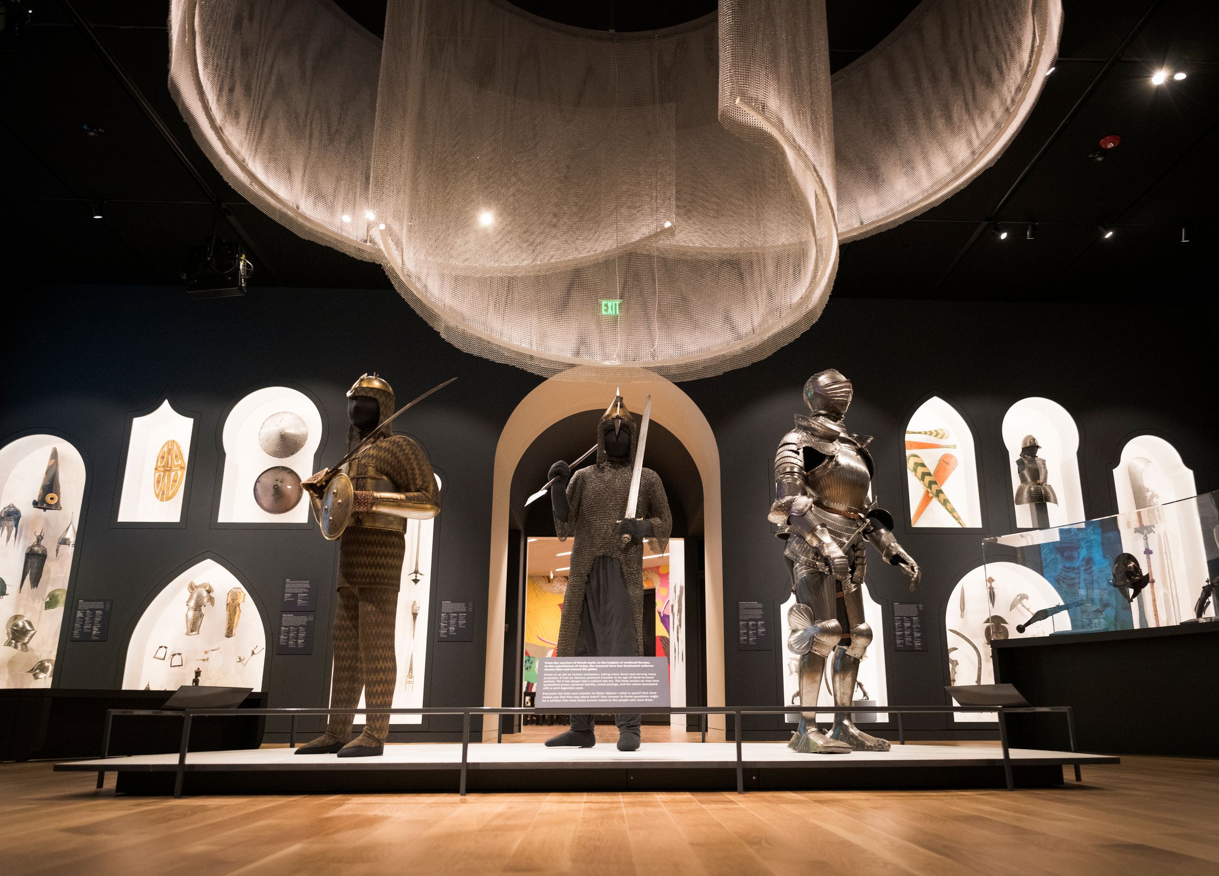 Theatrical stage setup with illuminated arches and flowing fabric displays showcasing medieval or fantasy-themed costumes.