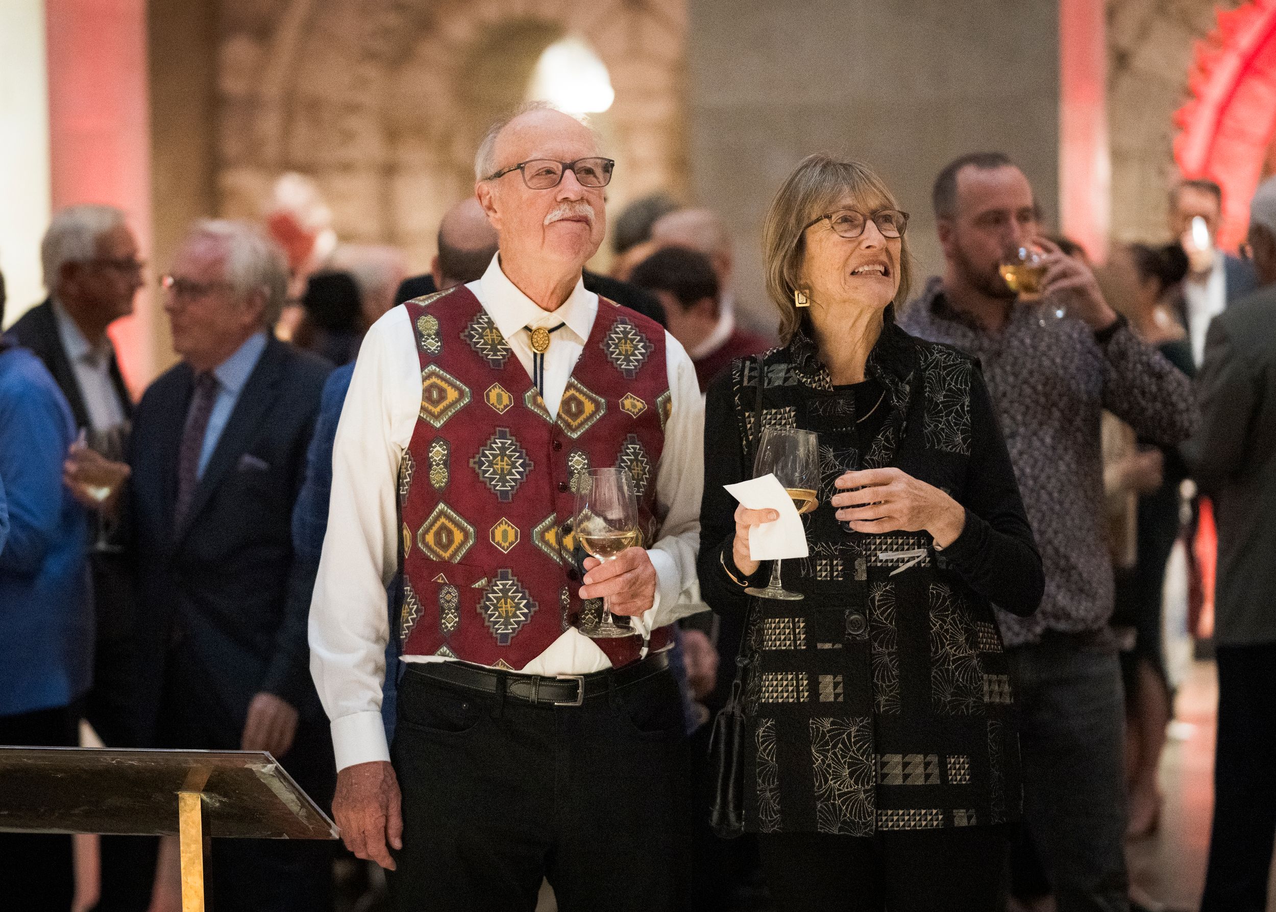 People in formal attire enjoy drinks and conversation at an elegant indoor social gathering.