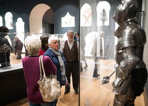 Gallery visitors viewing artwork and exhibits in a museum space with dark walls and spotlighting.