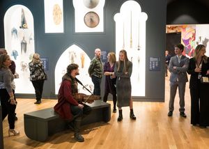 Gallery visitors observe illuminated art displays and installations in a museum exhibition space.