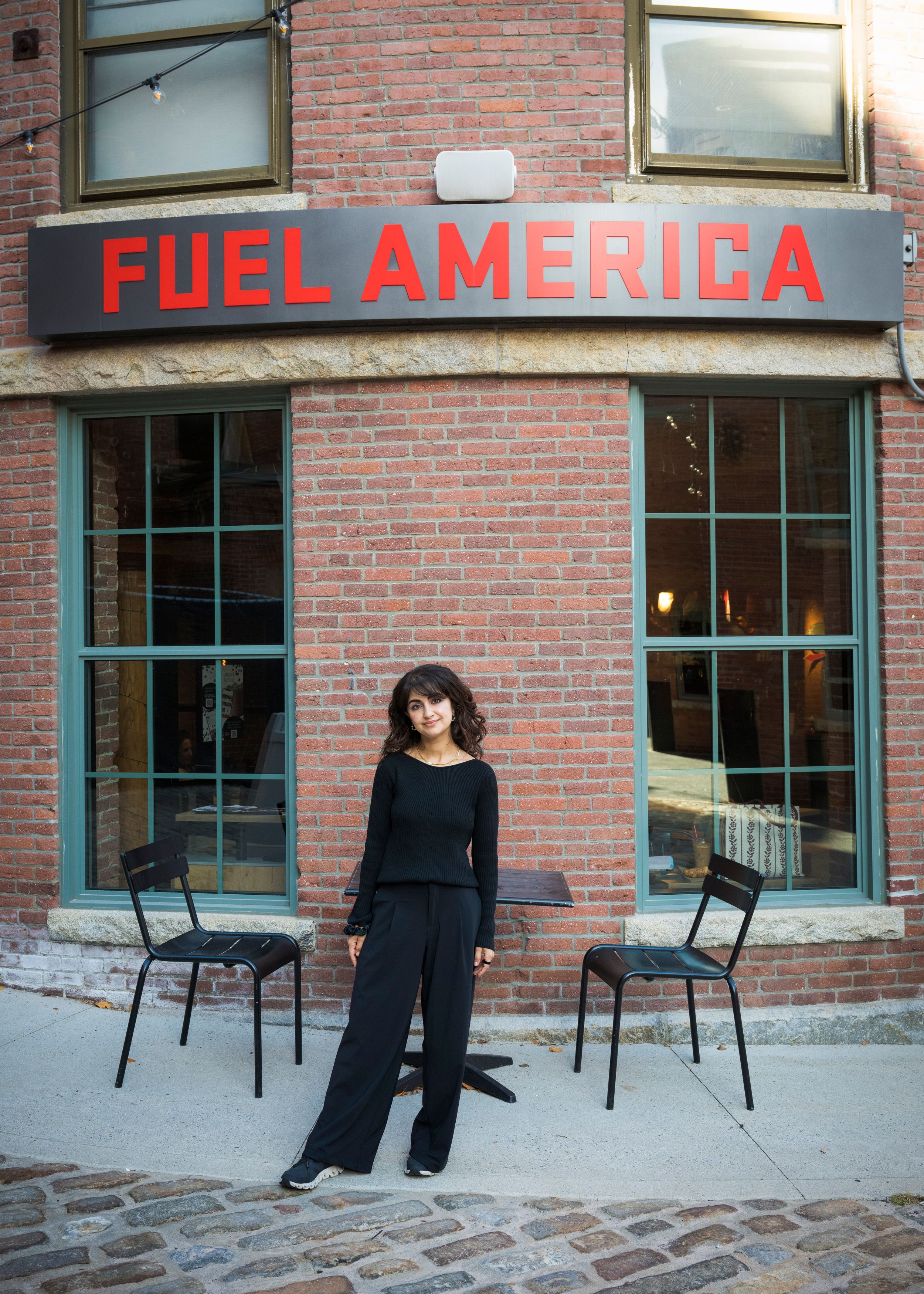 A series of empty black metal chairs arranged in front of a brick building with 'FUEL AMERICA' signage.