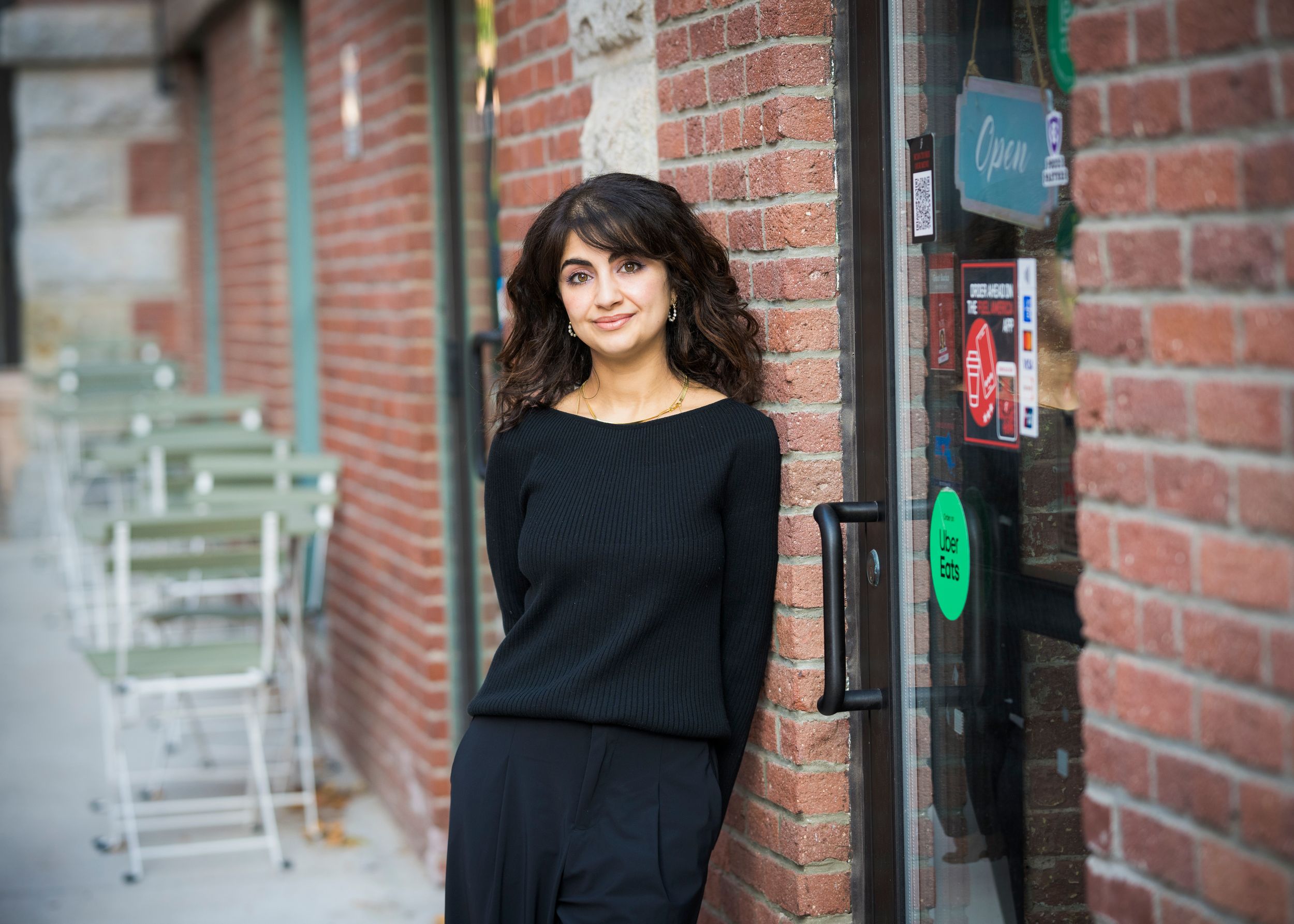 A person in a black sweater poses against a brick wall in an urban setting.