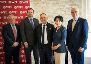 A group of five people in business attire stand together in front of a wall with WPI logos.