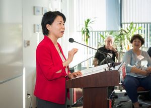 Speaker in red blazer presenting at a podium during a professional event.