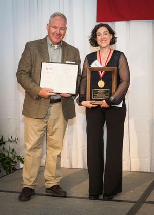 Award ceremony with people in formal attire exchanging certificates and plaques on stage.