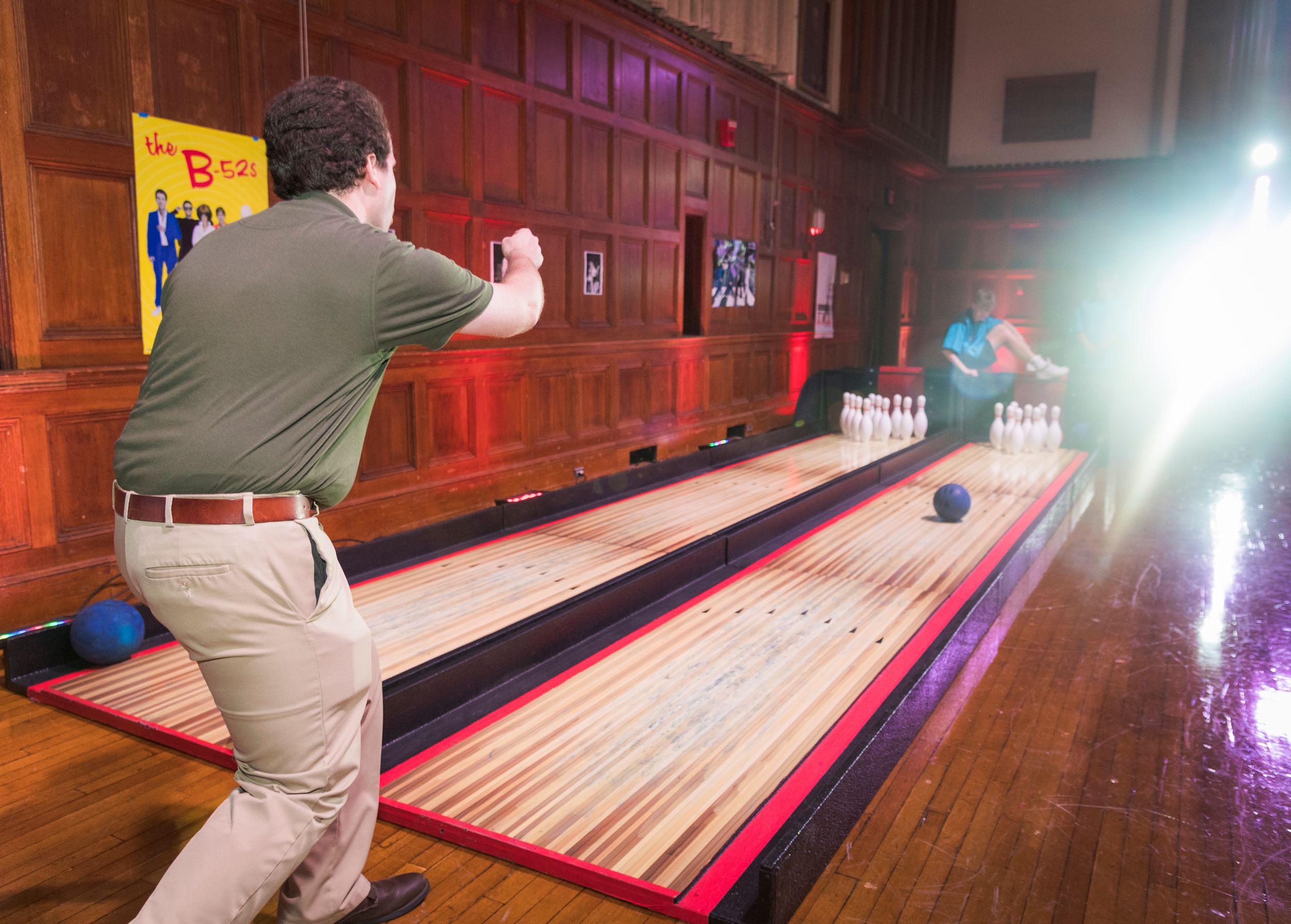 A person bowling on a vintage wooden lane with colorful lighting in an indoor entertainment venue.