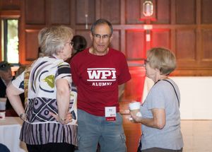 Three people having a conversation at an event, with one person wearing a red WPI Alumni t-shirt.