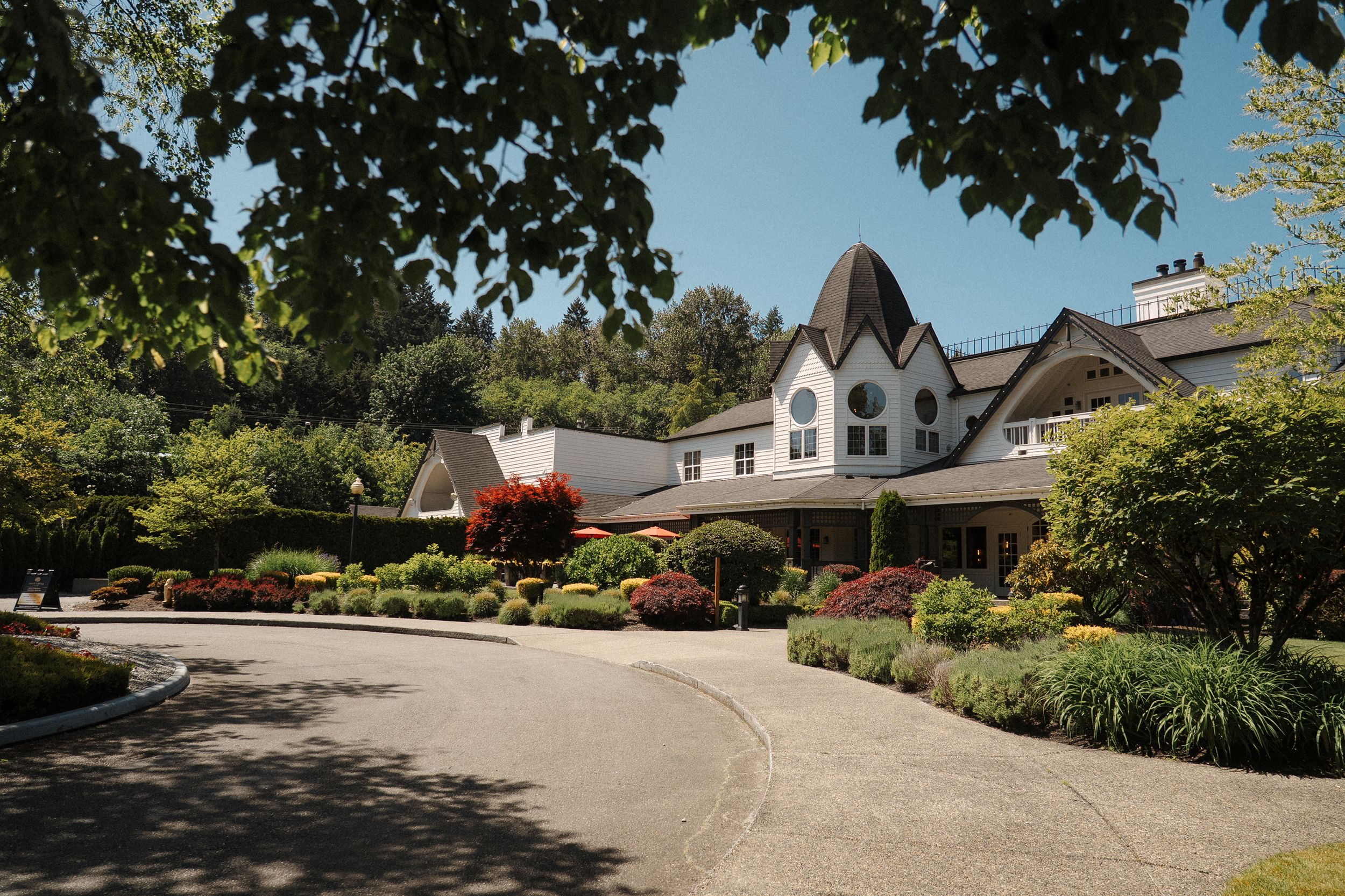 Elegant white Tudor-style building with landscaped gardens and circular driveway entrance on a sunny day.