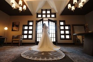 Elegant wedding dress train spreads across rustic wooden floor in sunlit room with vintage windows.