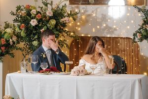 Wedding reception head table decorated with floral arrangements and string lights.