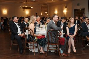 Wedding reception guests gather in an elegant venue with warm lighting and chandelier during evening celebrations.