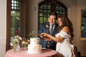 A couple cutting their white tiered wedding cake together at an elegant reception venue.