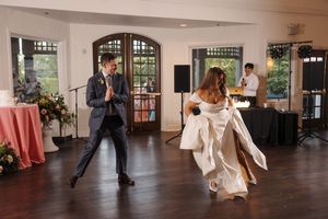 Wedding couple performs first dance on polished wooden floor in elegant ballroom with arched windows.