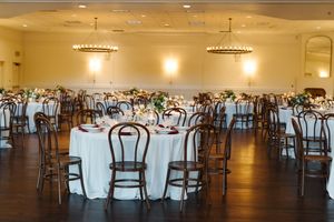 Elegant wedding reception venue with round tables, wooden chairs, and warm lighting.