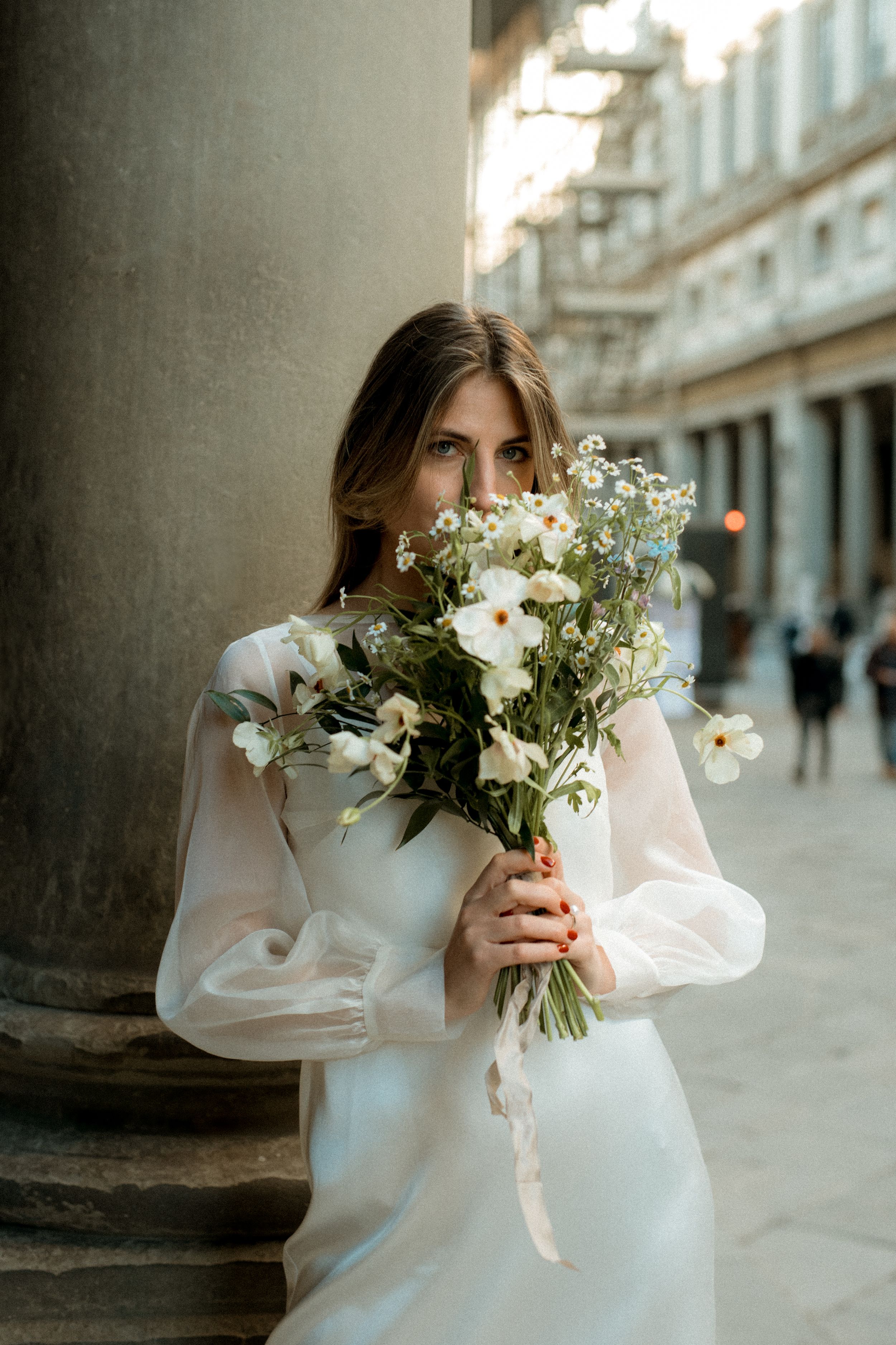 A wedding photo showing bride in a white Anni Ruuth dress holding a flower bouquet in front of her face in Florence, Italy.