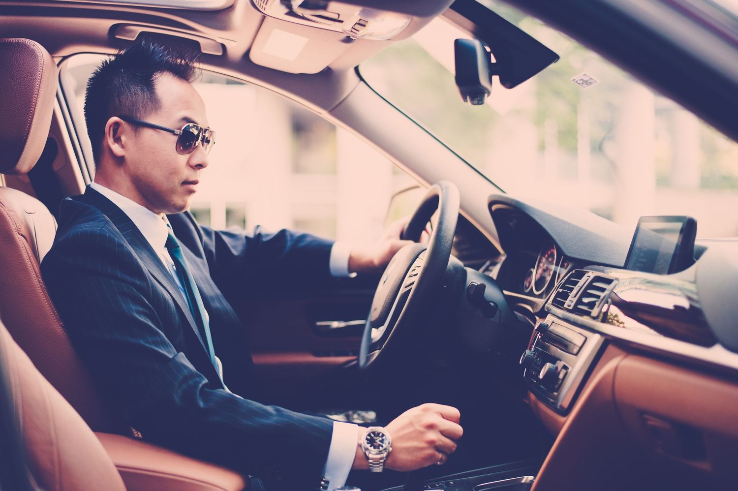 Professional in a business suit sits behind the wheel of a luxury car interior.