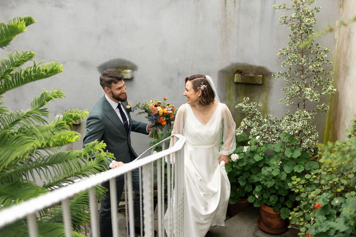 A couple stands together in a lush garden setting during an intimate outdoor wedding ceremony.