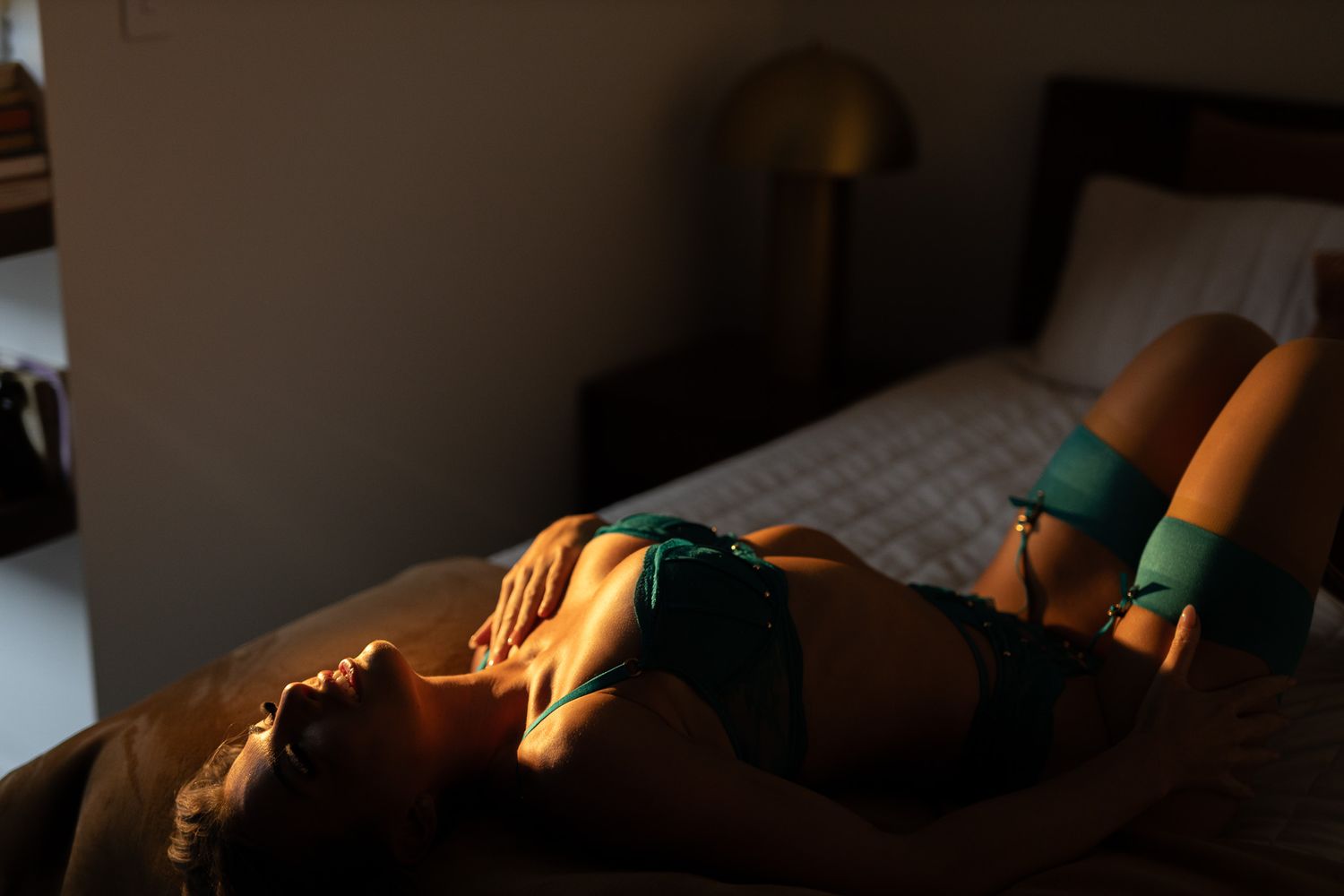 Artistic boudoir photograph with dramatic moody lighting in bedroom setting.