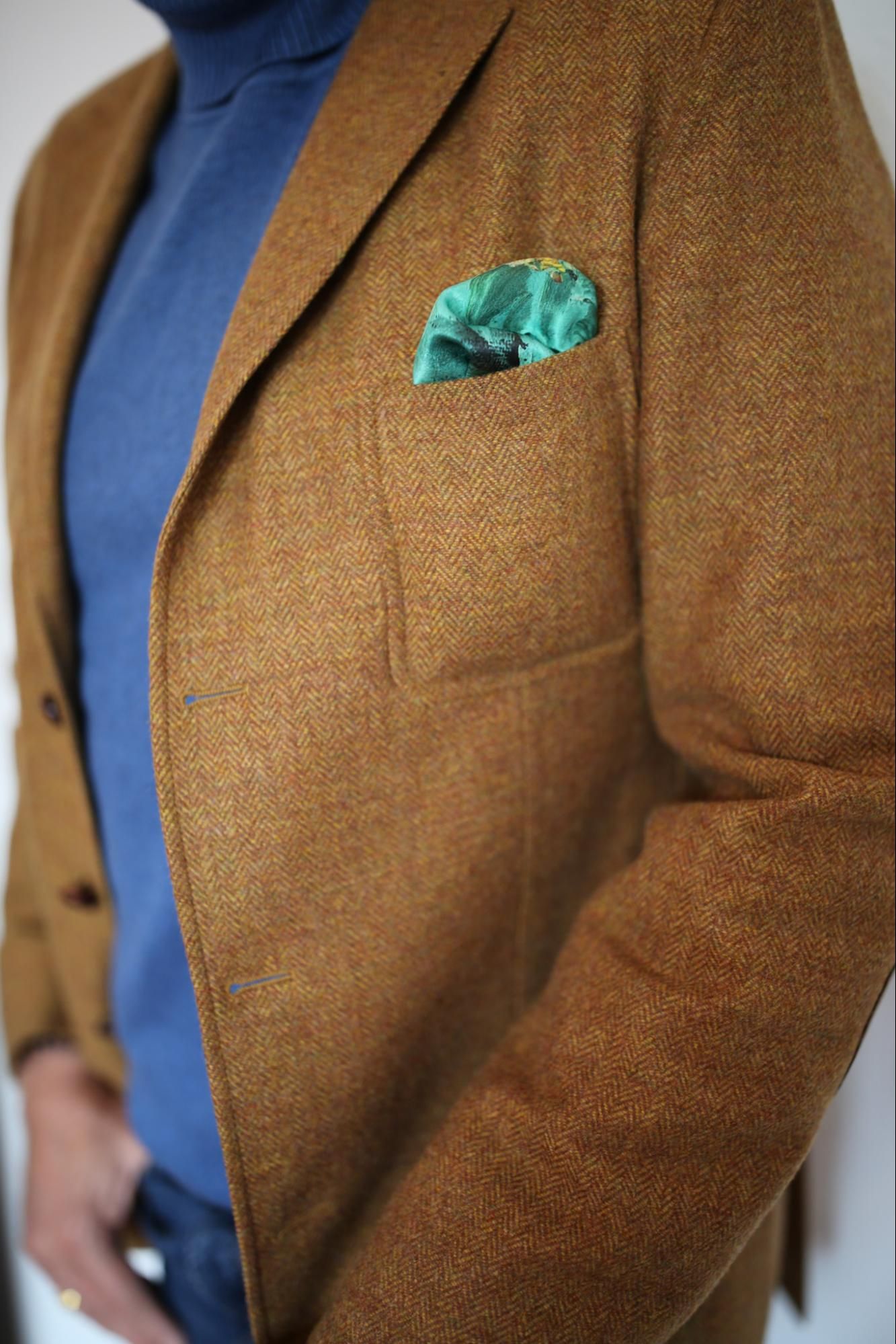 Close-up of brown tweed blazer with teal pocket square and blue shirt showing classic menswear styling.