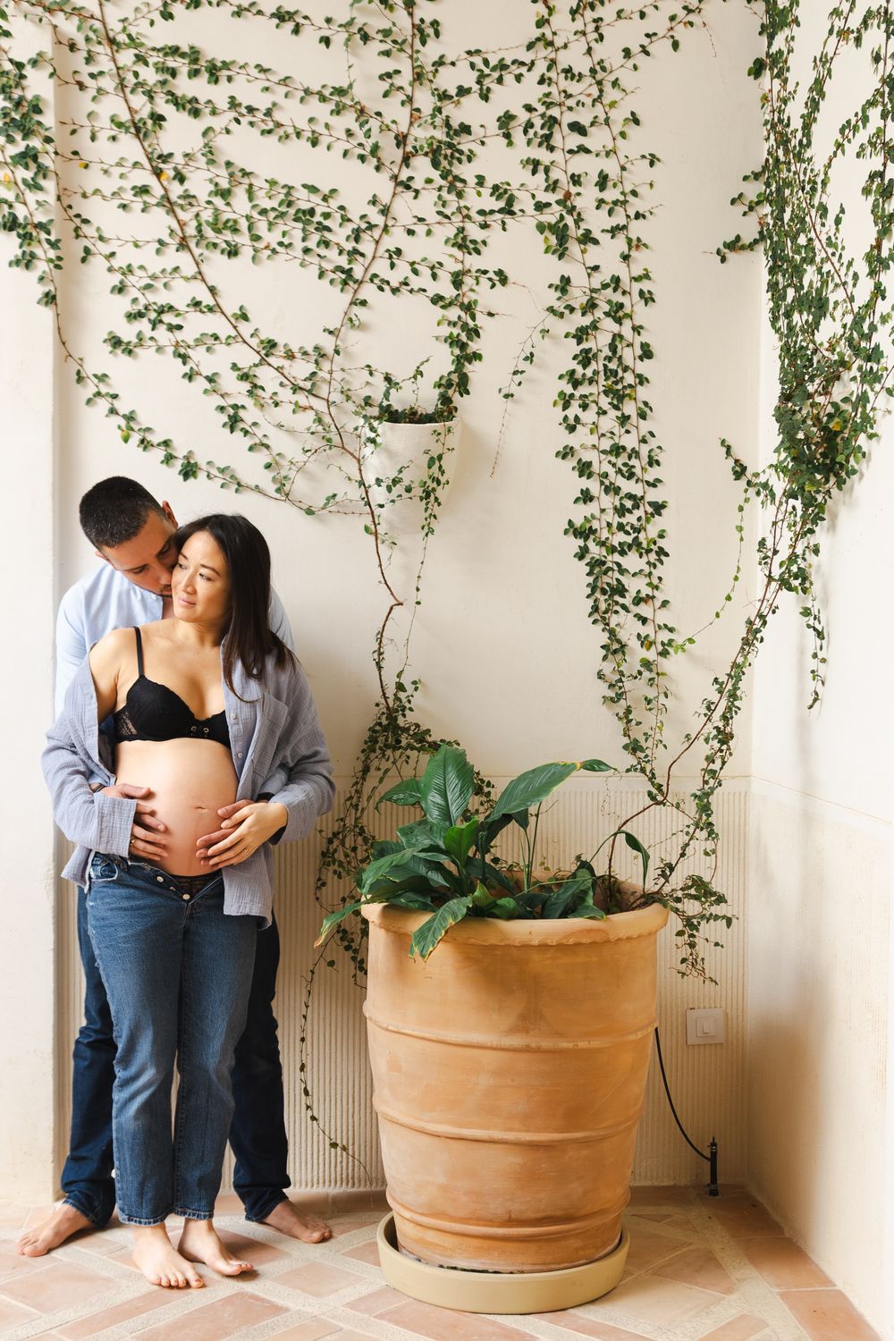 A romantic couple embraces near terracotta planters with climbing vines and greenery in a bright indoor space.