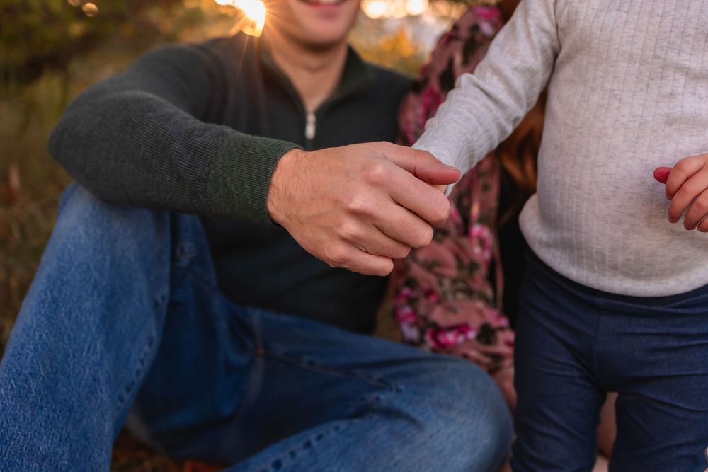 A close-up shot of dad holding toddler daughters hand during an outdoor moment at sunset.