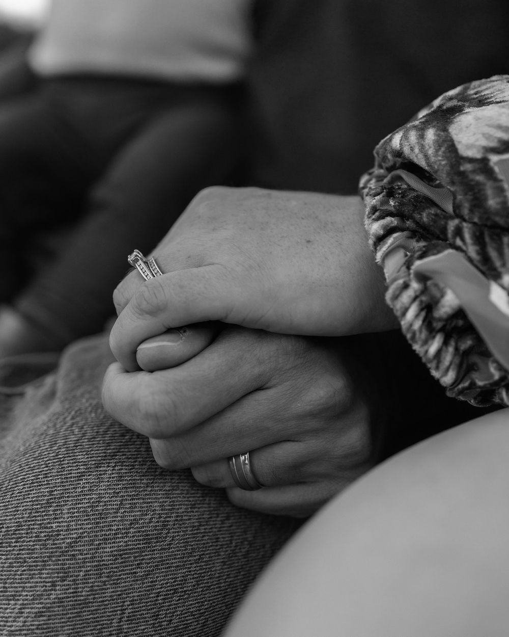 Black and white close-up image of hands gently clasped together resting on textured fabric.