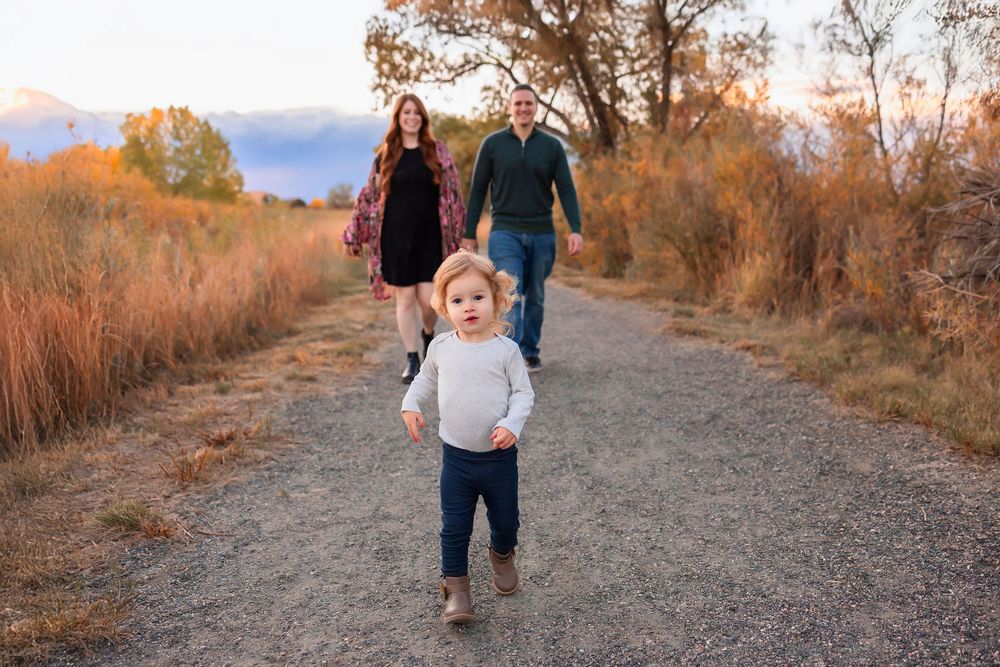 Family walks together on a scenic autumn trail surrounded by golden foliage and mountain views at sunset.