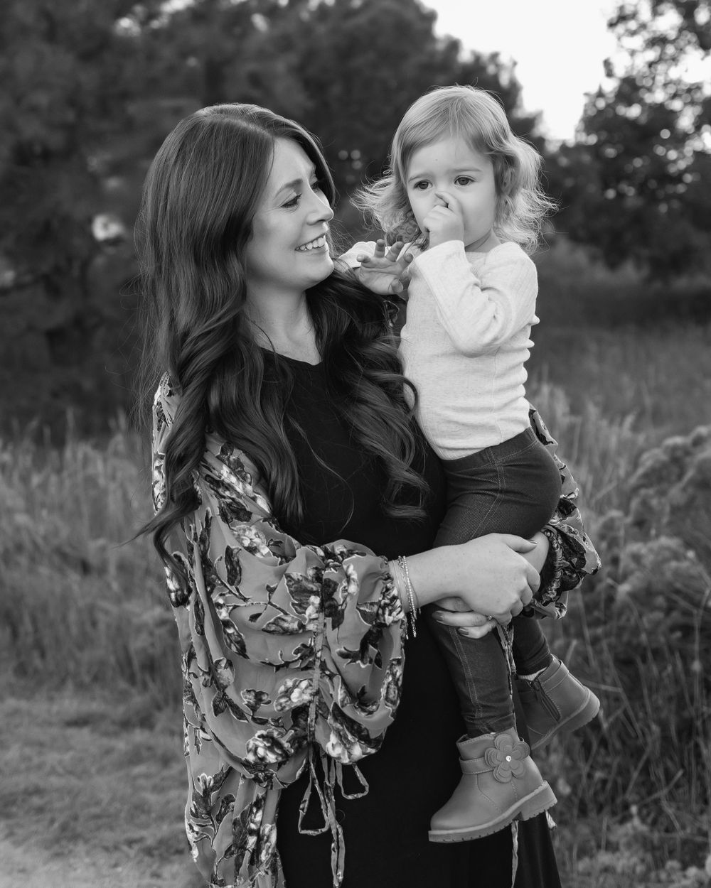 Black and white photo showing a tender moment between mother and toddler daughter outside in a natural outdoor setting.