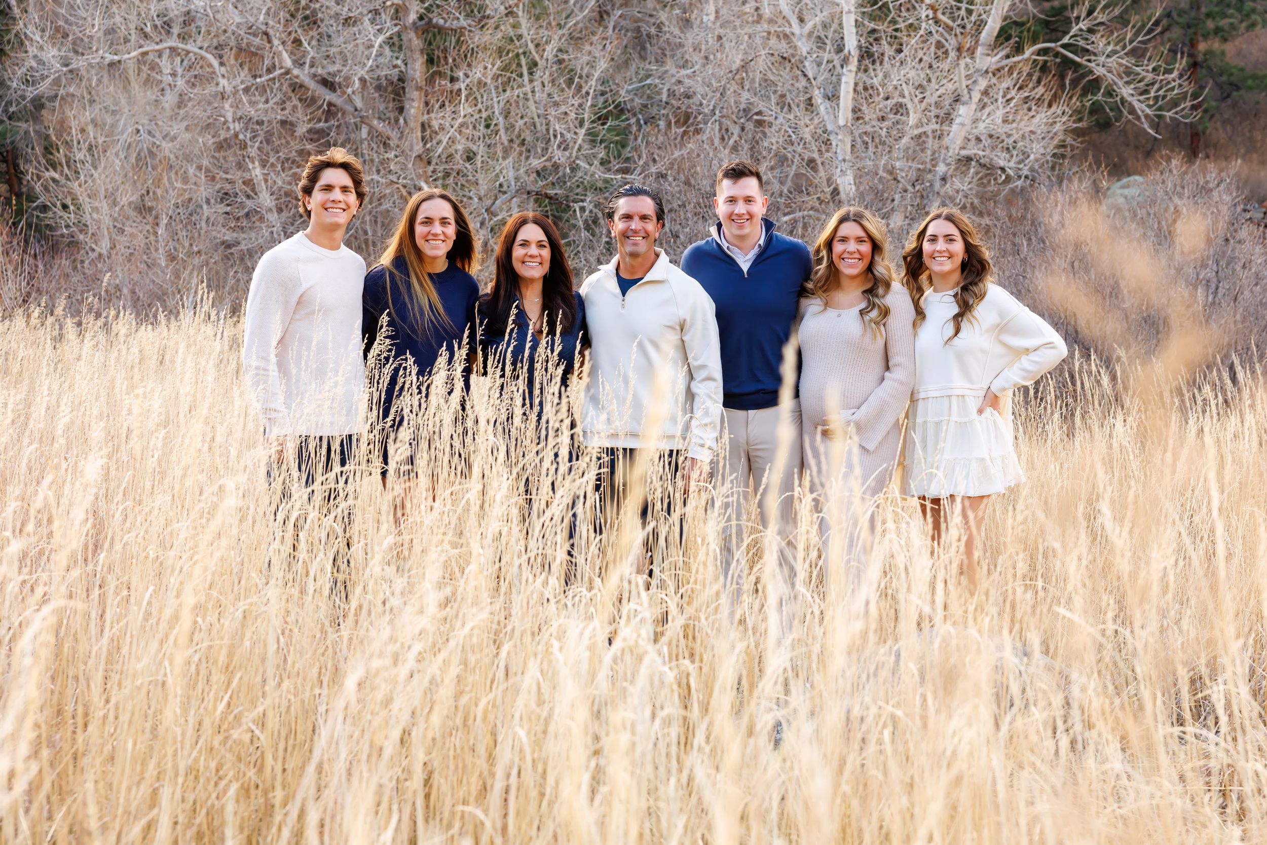 A group of people wearing white and blue outfits stand together in a field of tall golden grass during autumn.