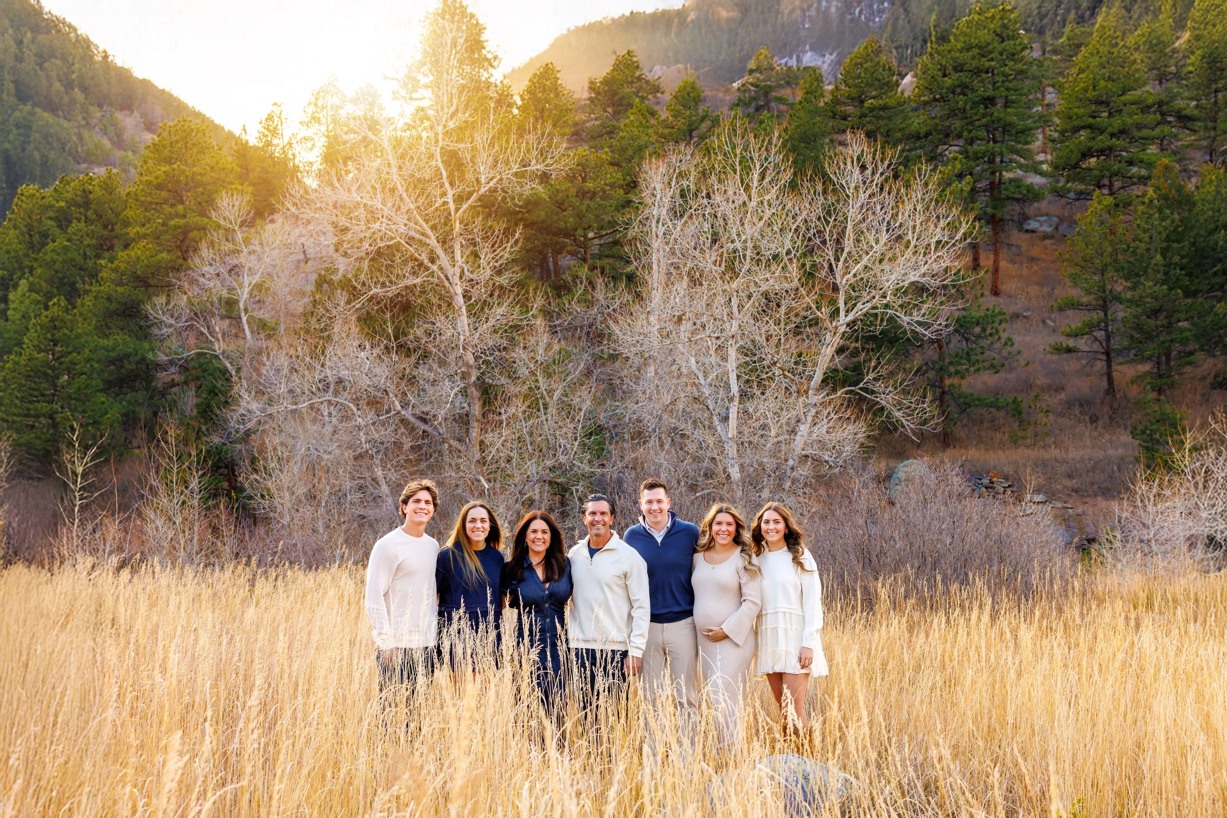 Group standing in golden sunlit meadow with mountain backdrop and tall grass during autumn sunset.