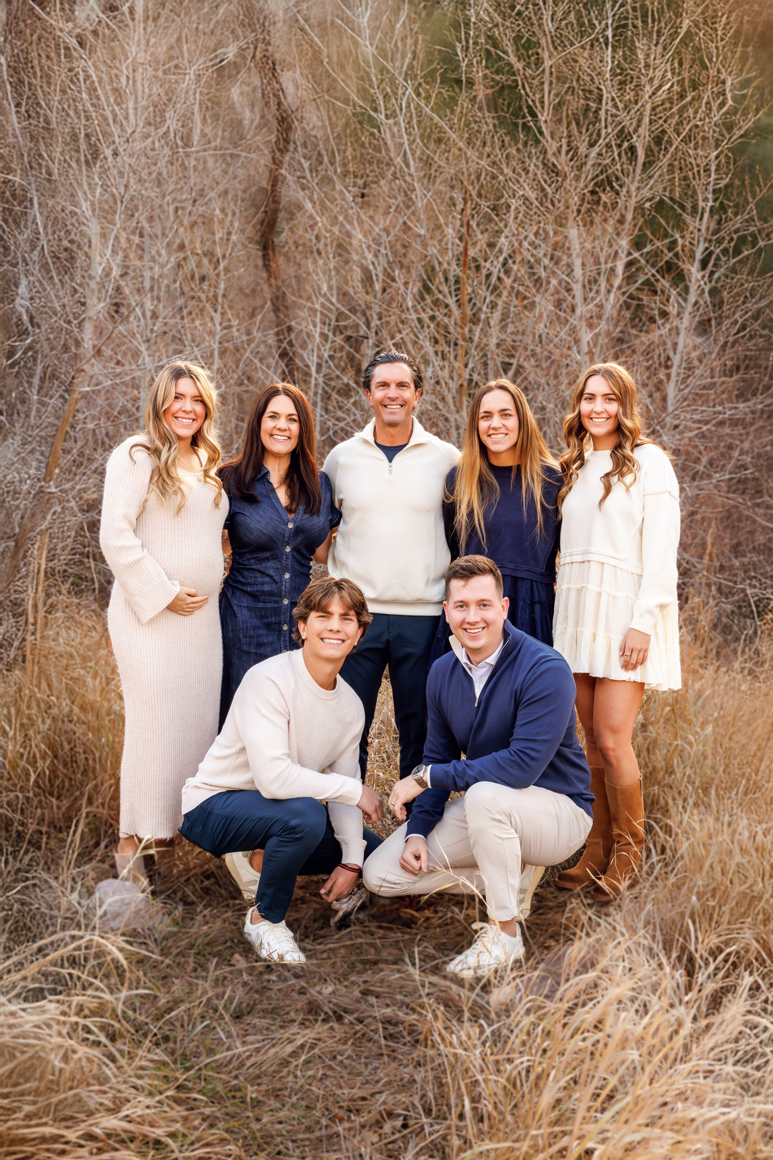 Family portrait series in coordinated navy and cream outfits posed together in natural tall grass setting.