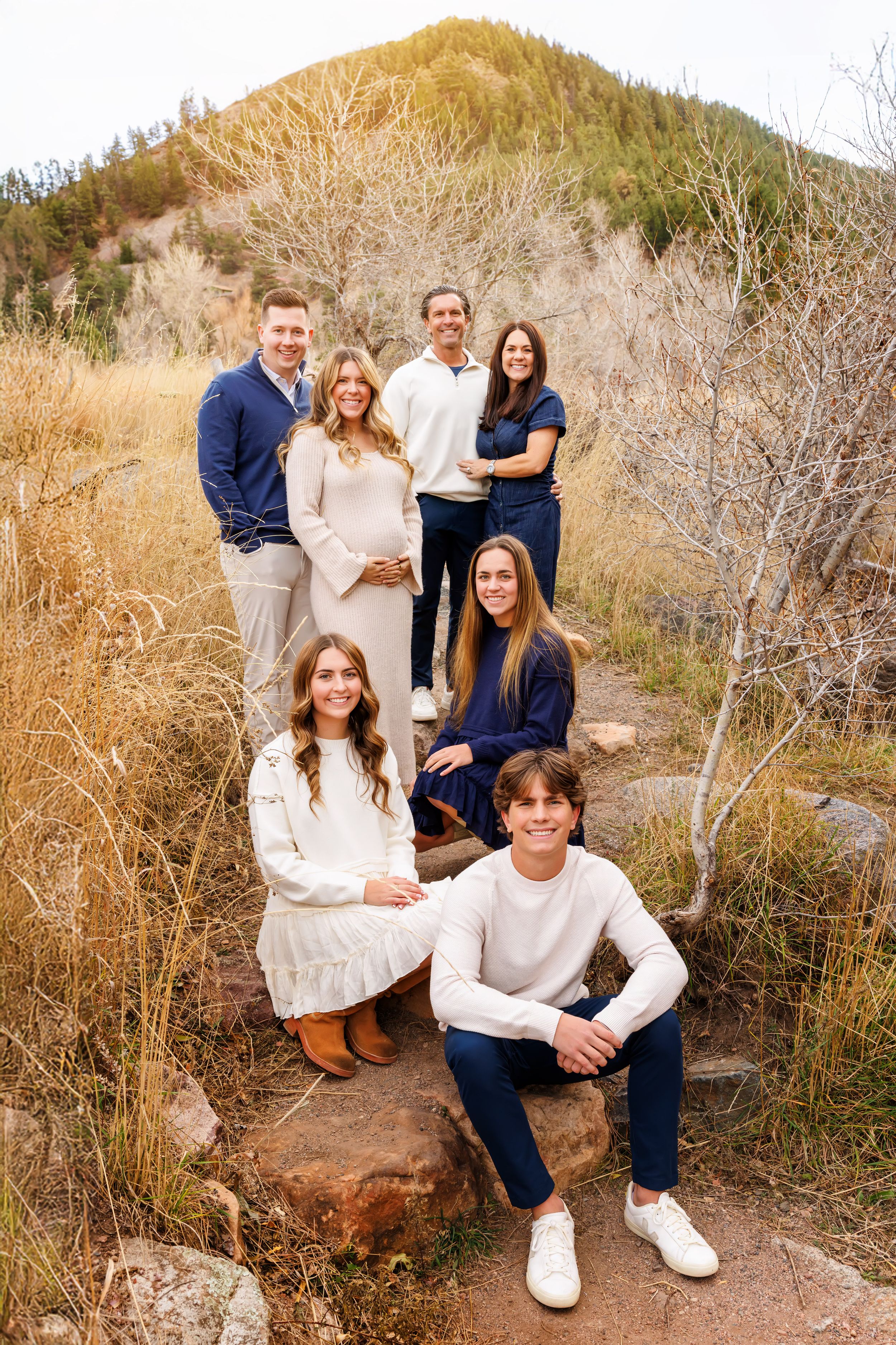 A group poses together in casual white and blue outfits against a backdrop of dried brush and foliage in nature.