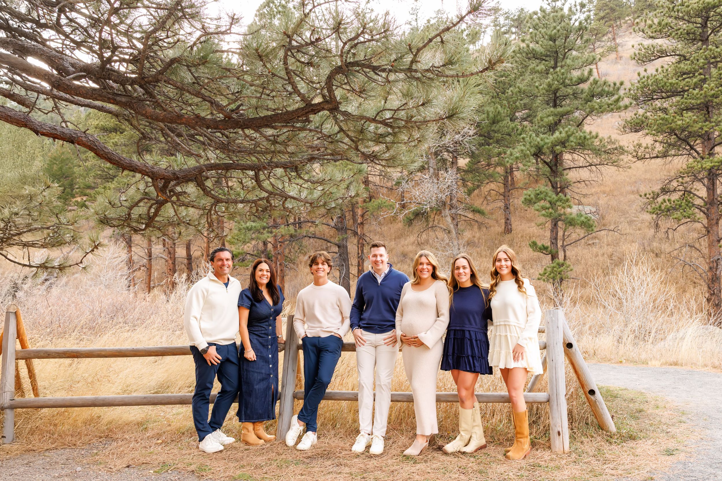 A group poses casually along a rustic wooden fence in coordinated blue and white outfits at an outdoor location.